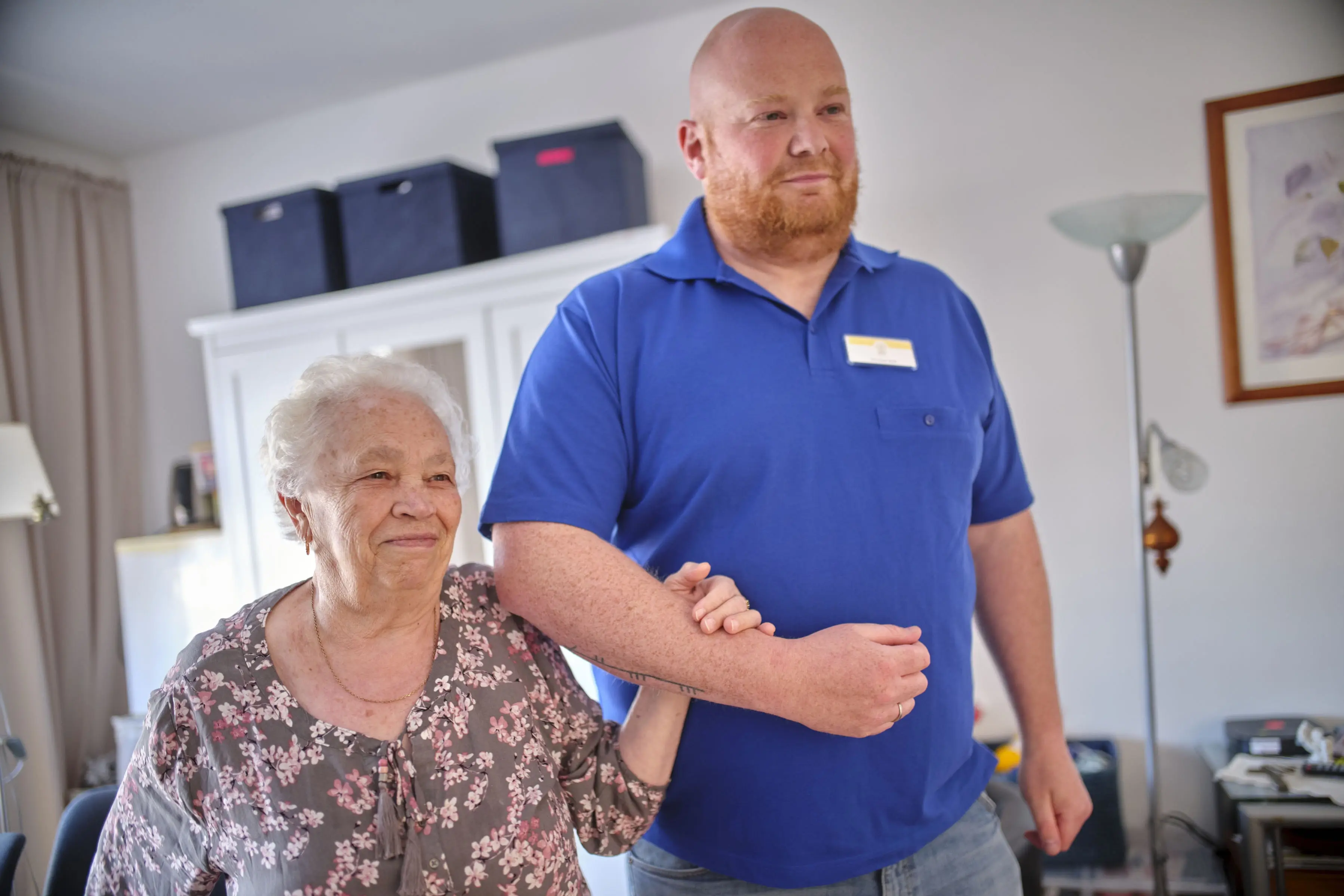 Seniorin geht mit Pflegekraft am Arm ein Stück