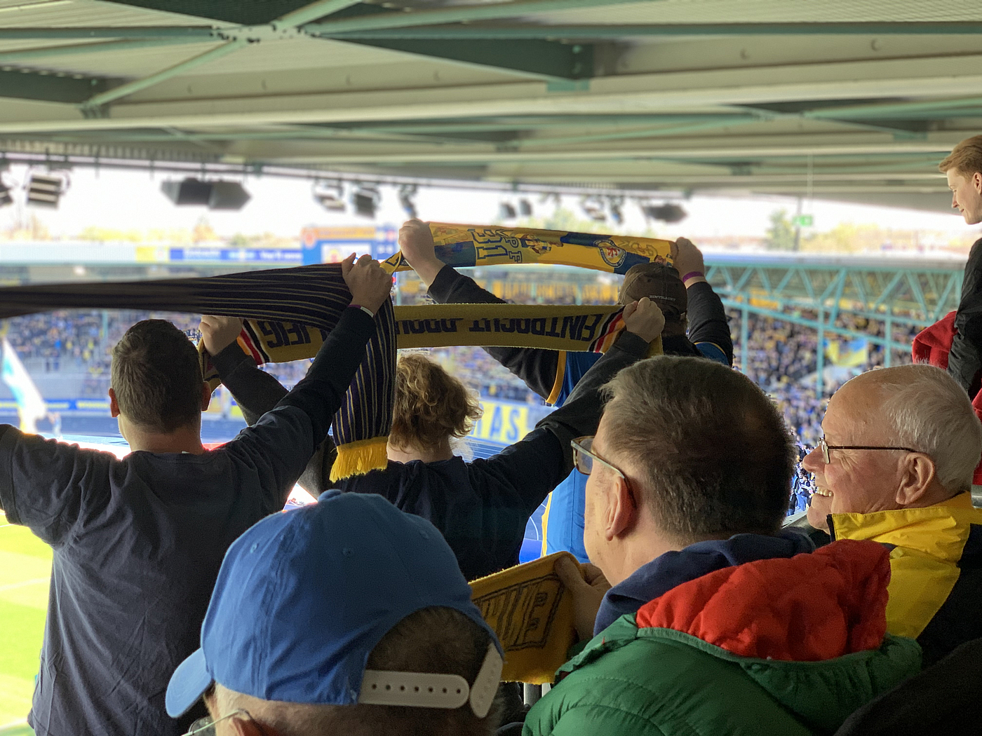 Fans jubeln den Fußballspielern zu und halten blau gelbe Schals in die Höhe