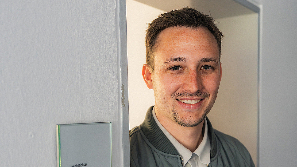 Jakob Richter lacht in die Kamera. Er steht in einem Türrahmen