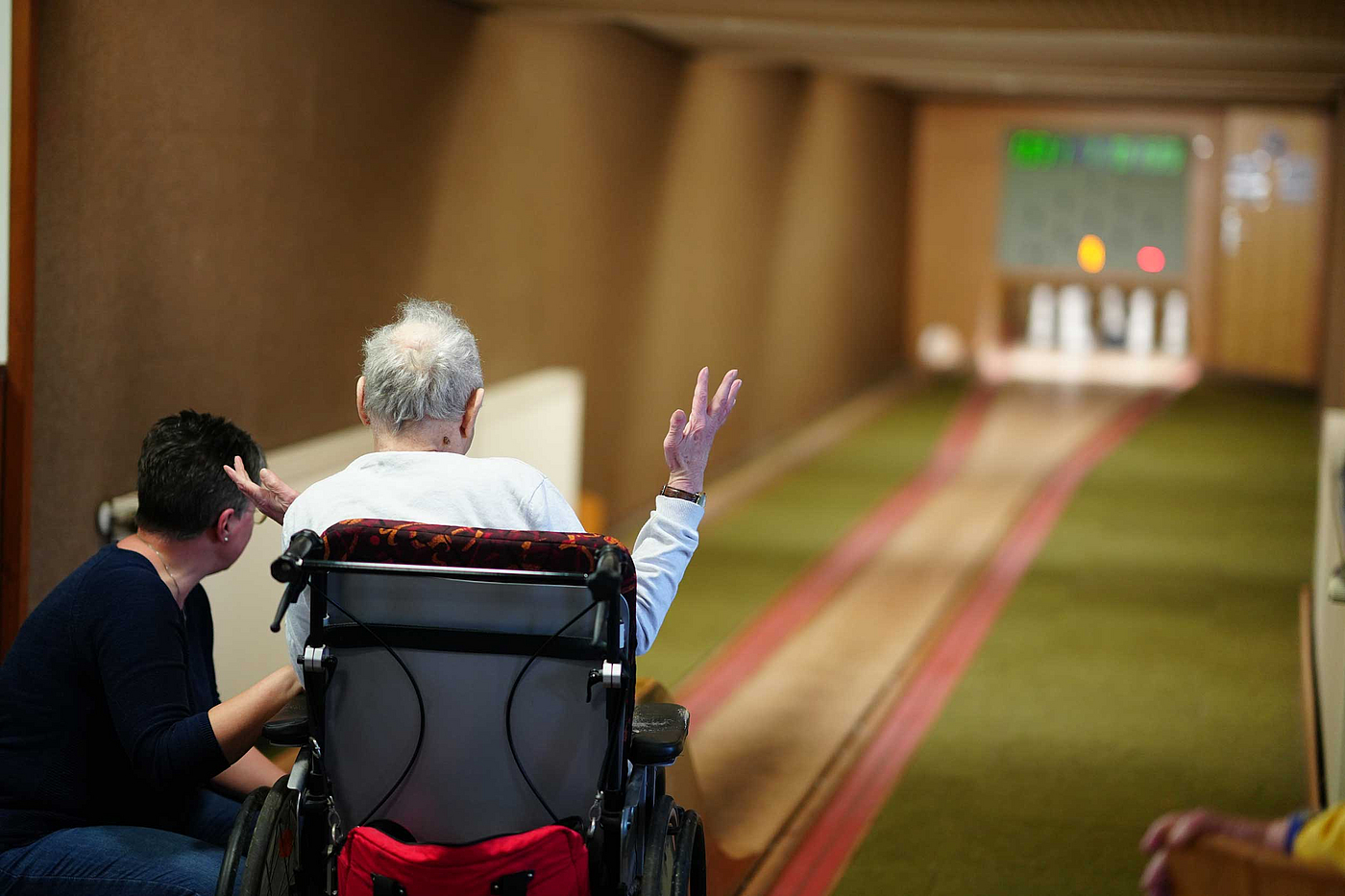 Älterer Mann im Rollstuhl kegelt zusammen mit seiner Betreuerin