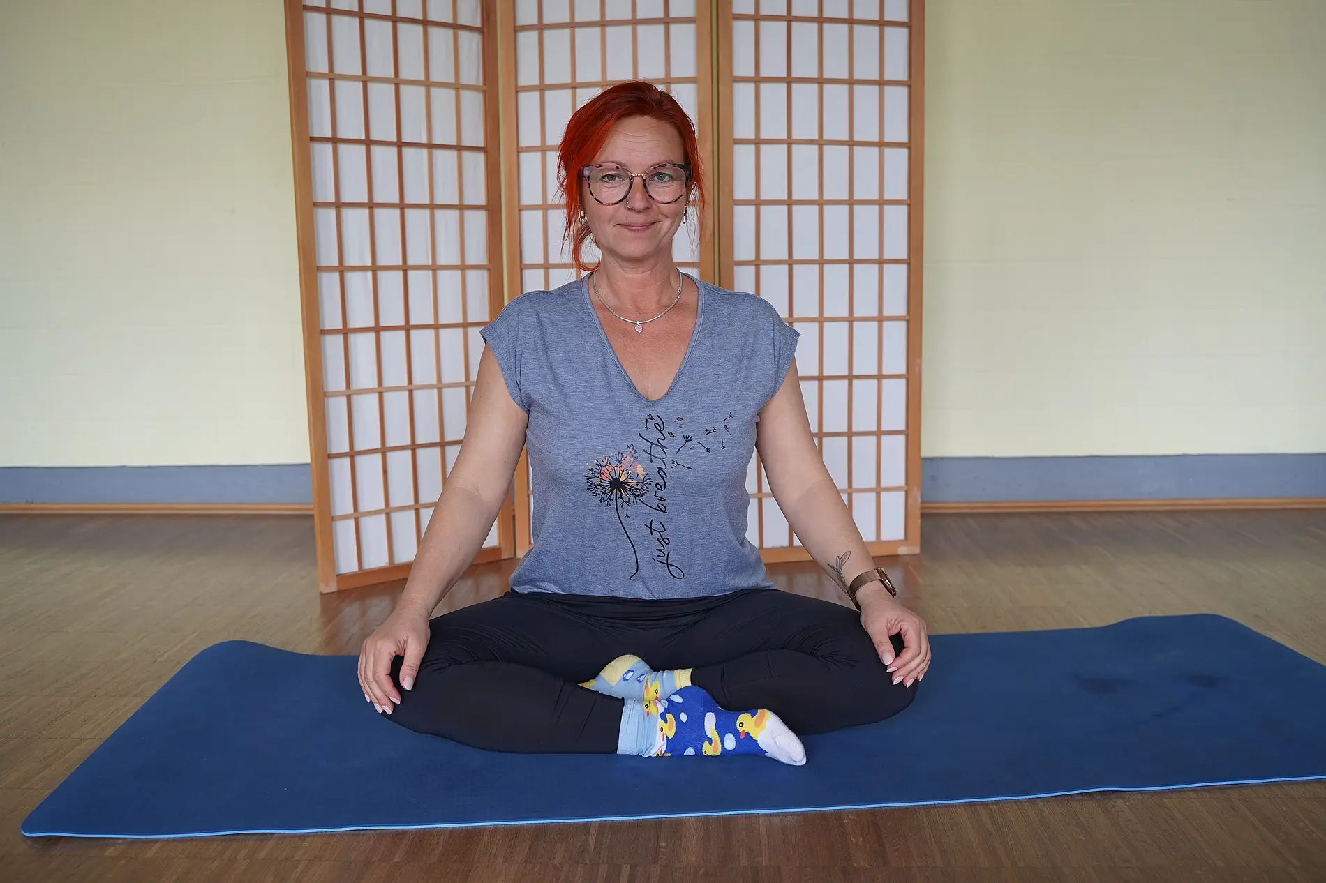 Brigitte Hube sitzt im Yogasitz auf einer Yogamatte.
