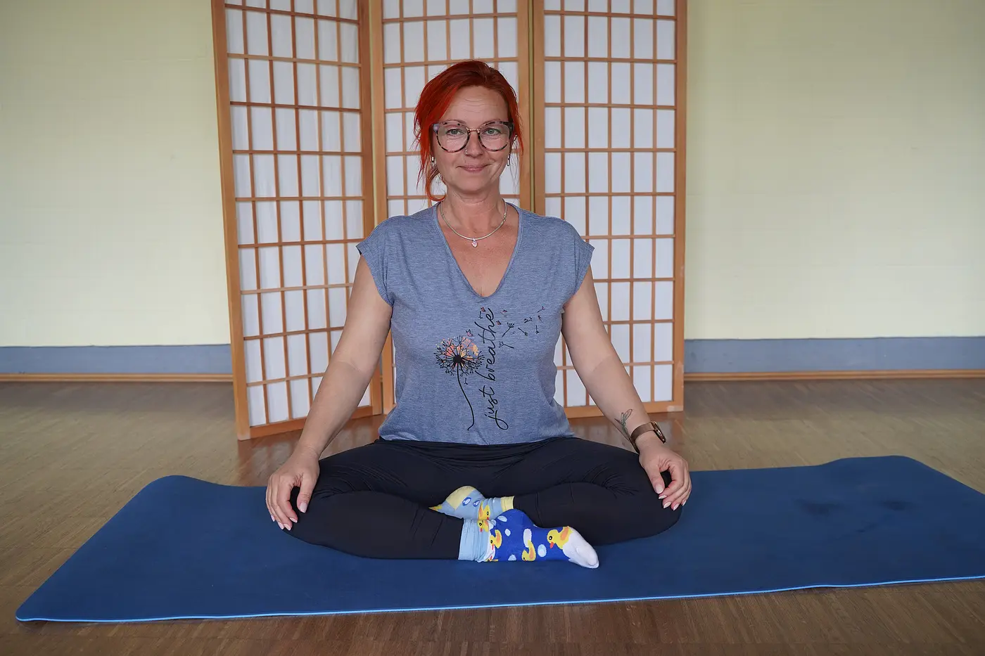 Brigitte Hube sitzt im Yogasitz auf einer Yogamatte.
