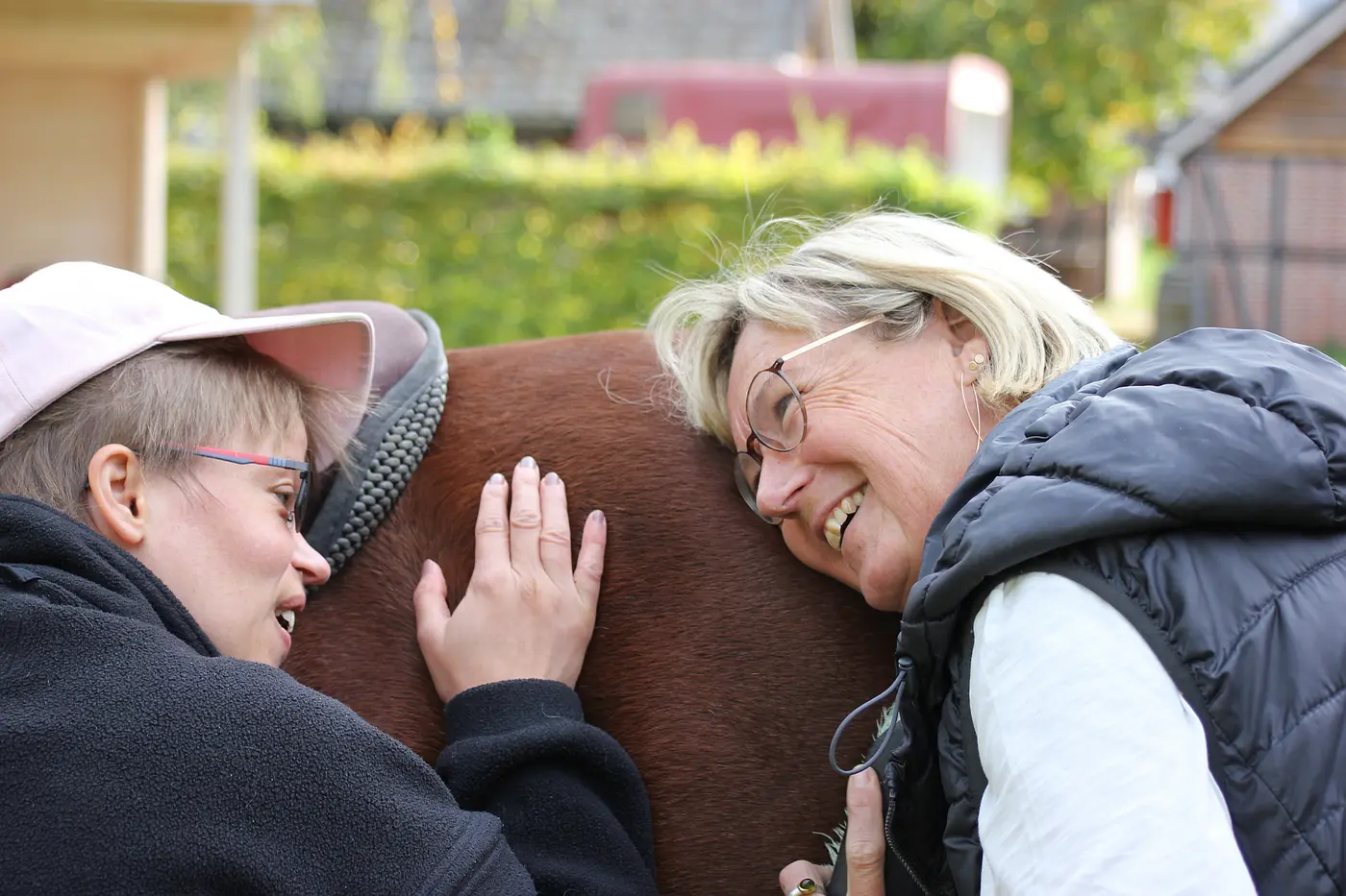 Zwei Menschen kuscheln mit einem Therapiepferd.