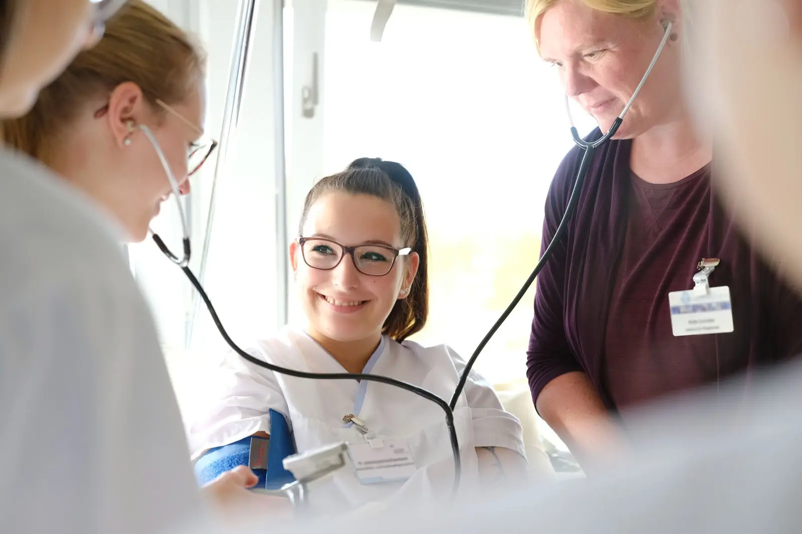 Lehrerin erklärt ihren Schülerinnen in der Pflegeausbildung wie man den Blutdruck misst 