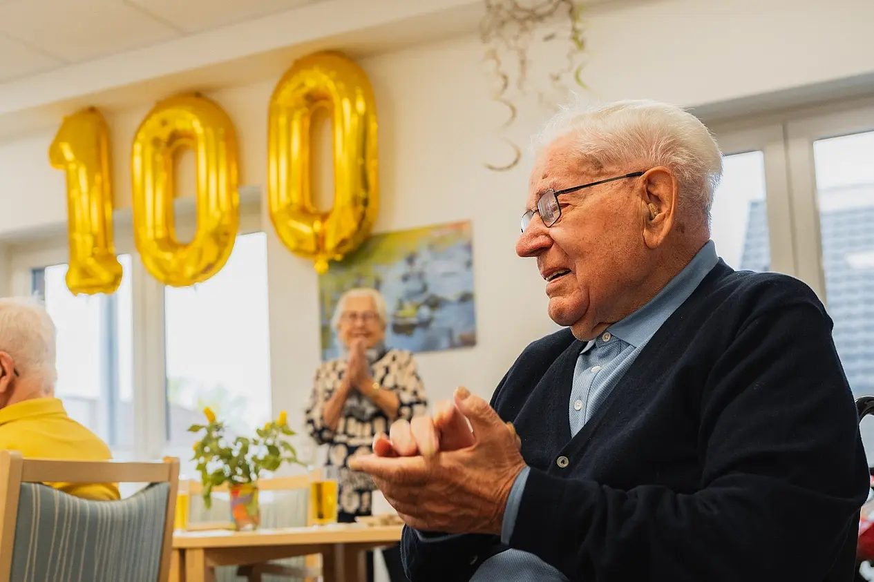 100ster Geburtstag - Mann schaut glücklich in den Raum. eine 100 aus Ballons im Hintergrund