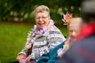 Eine Seniorin mit bunter Blumenkette lacht.