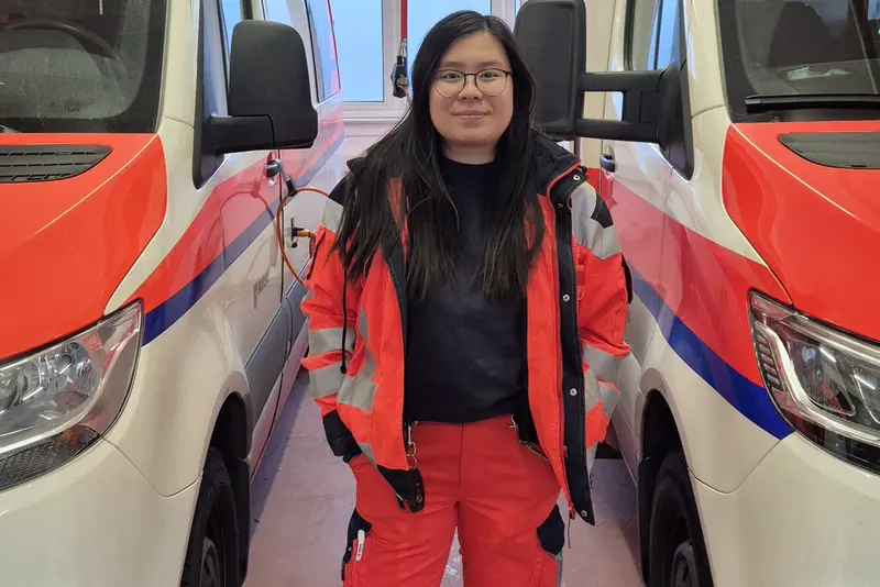 Junge Frau beim Rettungsdienst in Arbeitskleidung zwischen zwei Rettungswagen