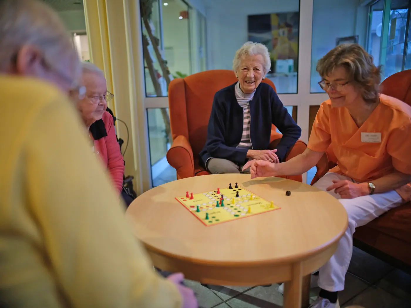 Drei Seniorinnen und eine Fachkraft spielen Mensch ärgere dich nicht.