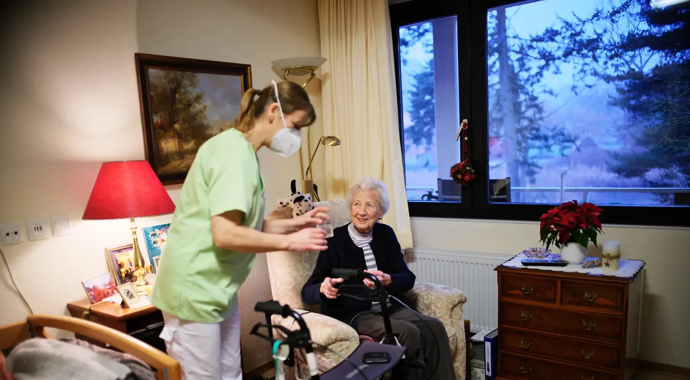 Pflegefachkraft betreut Seniorin in ihrem Zimmer im Pflegeheim St. Vitus