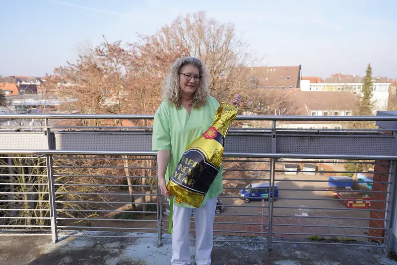 Cornelia Hoppe steht mit einem großen Ballon, der wie eine Sektflasche geformt ist, auf einem Balkon des Senioren- und Pflegezentrums Bethanien in Braunschweig.