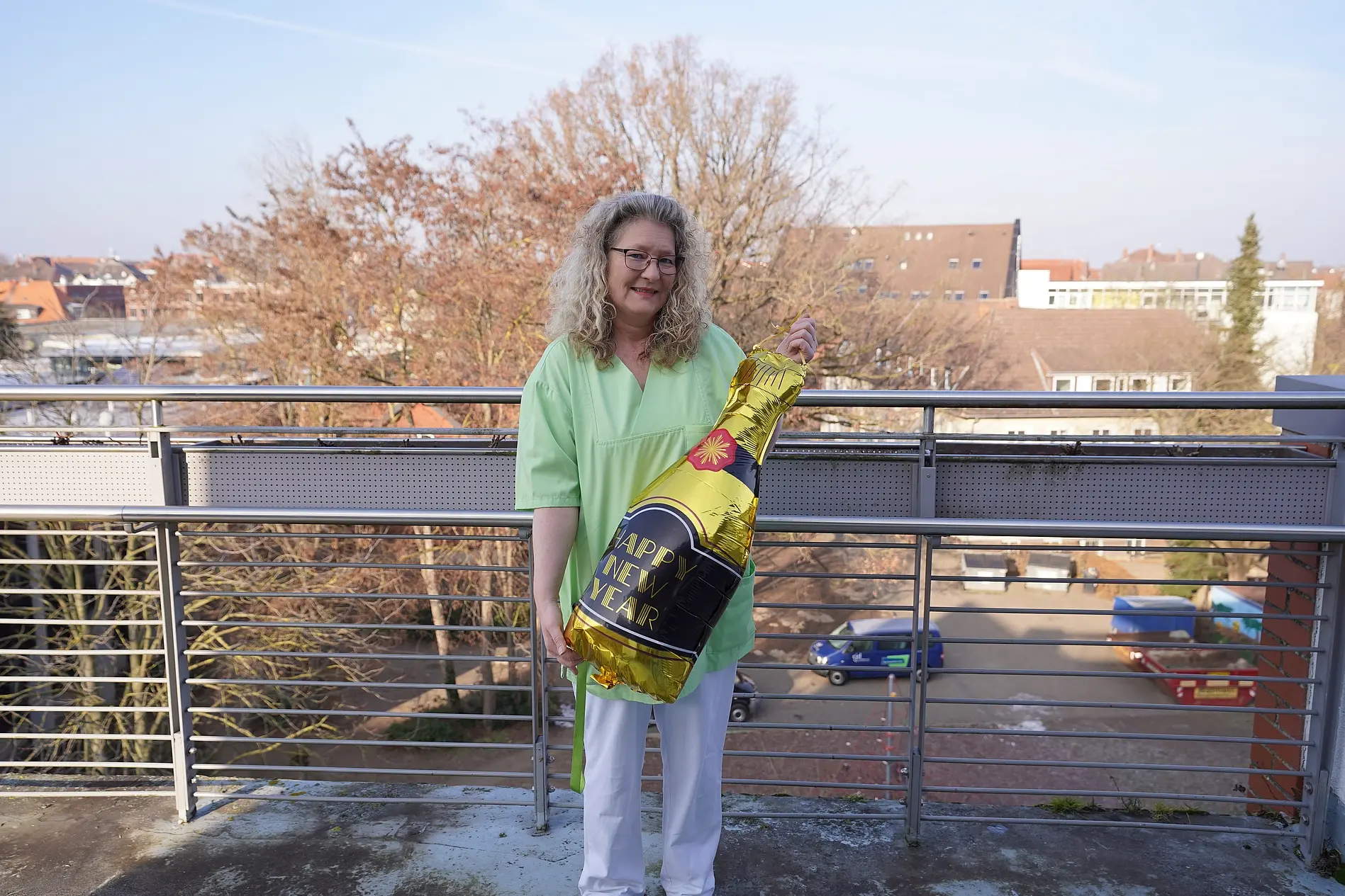 Cornelia Hoppe steht mit einem großen Ballon, der wie eine Sektflasche geformt ist, auf einem Balkon des Senioren- und Pflegezentrums Bethanien in Braunschweig.