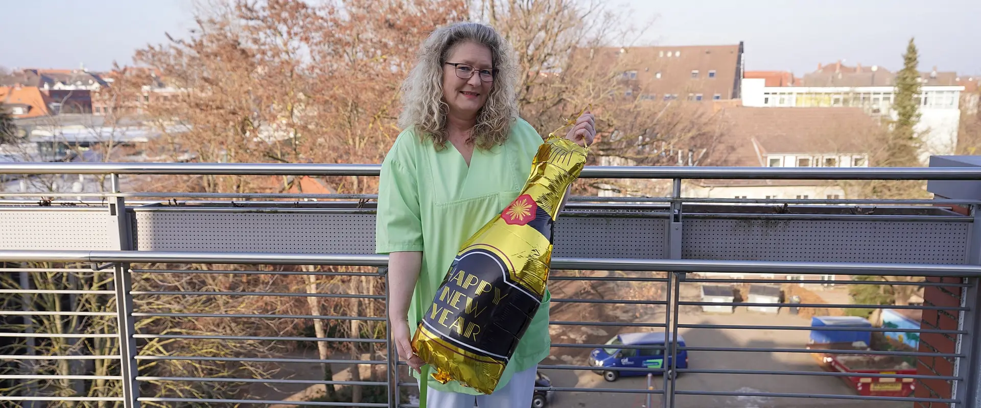 Cornelia Hoppe steht mit einem großen Ballon, der wie eine Sektflasche geformt ist, auf einem Balkon des Senioren- und Pflegezentrums Bethanien in Braunschweig.