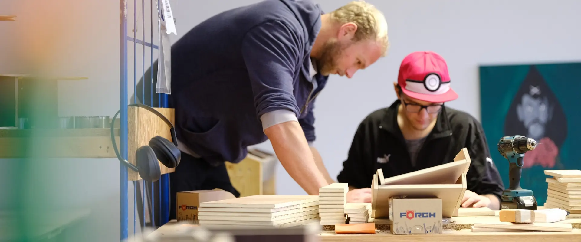 Fachanleiter beugt sich zu einem Teilnehmer, der etwas aus Holz baut