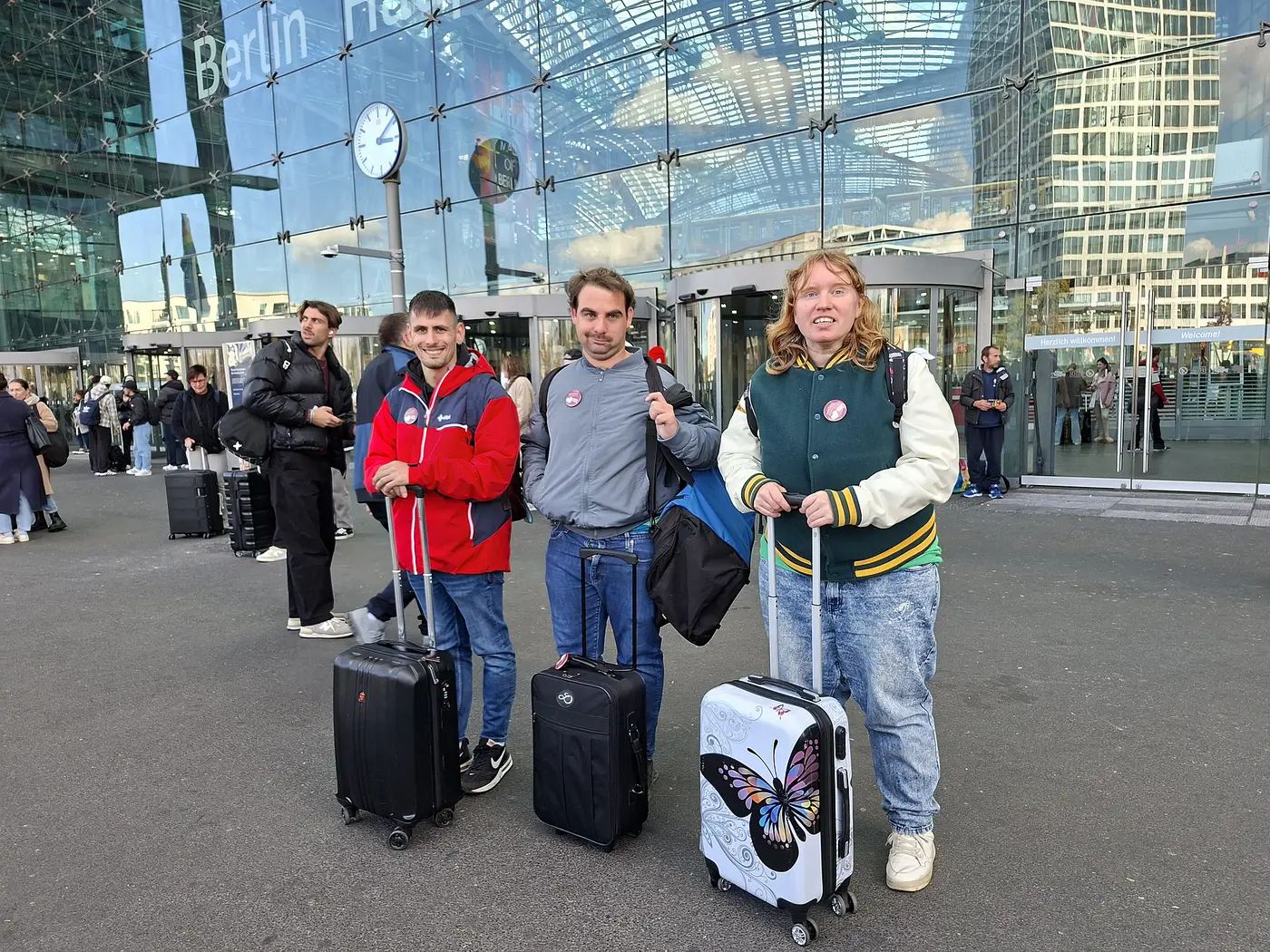 Menschen stehen mit einem Koffer vor einem Bahnhof.