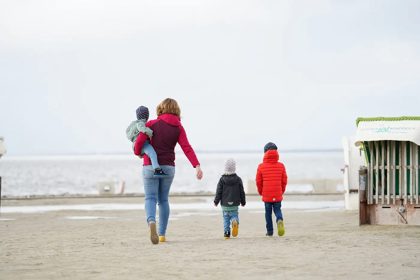 Eine Mutter und ihre Kinder gehen an einem Strand spazieren.