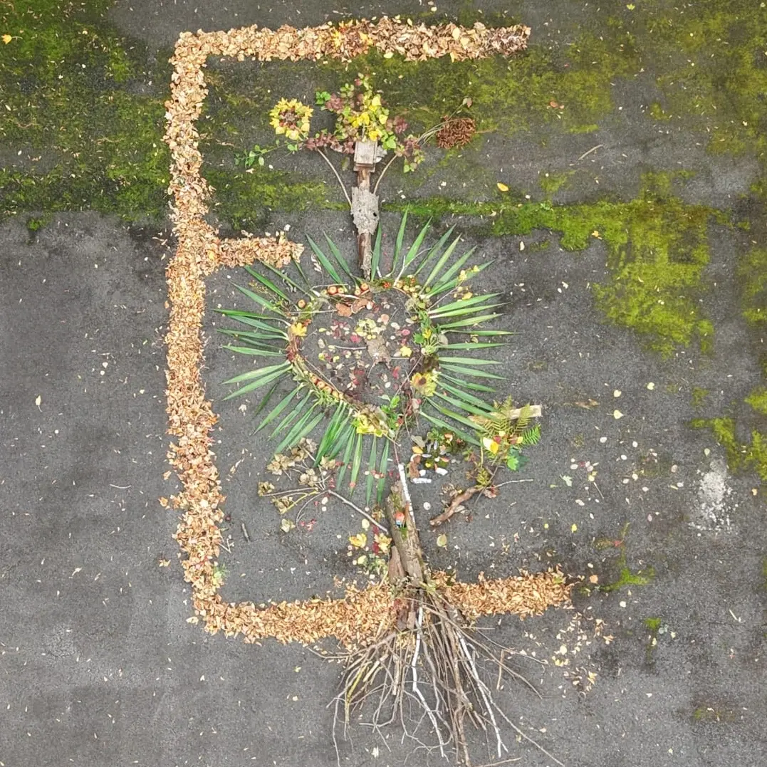 Land Art Kunstwerk aus Stöcken und Blättern. Mit Baum mit Herzkrone und einem großen E aus Blättern